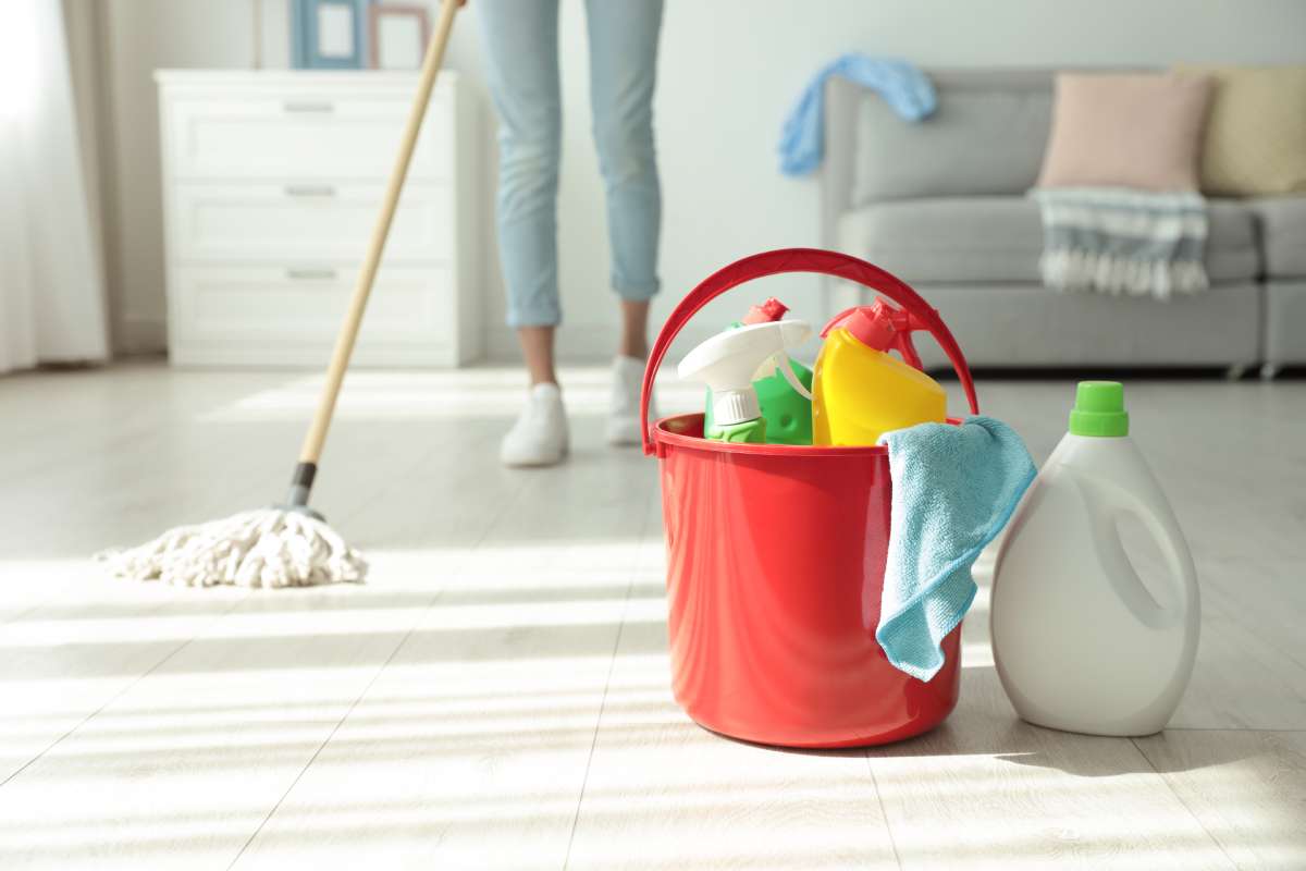 A woman mopping her floor with a string mop behind a bucket of cleaning supplies.