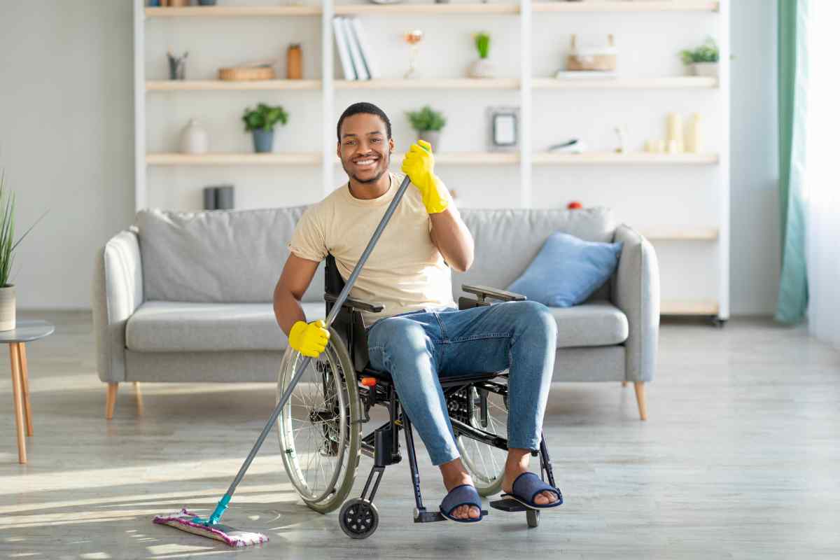 A man in a wheelchair wearing yellow gloves and mopping the floor.