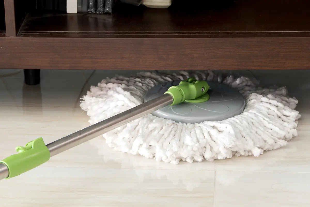 A green spin mop cleaning under furniture.